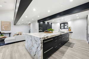 Kitchen with dark cabinetry, a large island, modern cabinets, beamed ceiling, and open floor plan
