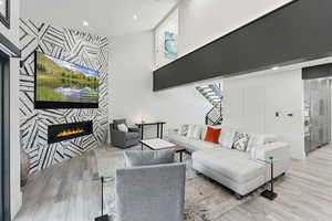 Living area with an accent wall, a tiled fireplace, light wood-style floors, stairway, and recessed lighting