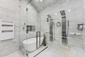 Bathroom featuring a freestanding bath, a marble finish shower, radiator, and tile walls