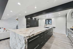 Kitchen with a spacious island, dark cabinets, open floor plan, light stone countertops, and recessed lighting