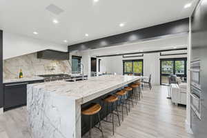 Kitchen featuring a large island, a breakfast bar area, tasteful backsplash, light stone countertops, and light wood-style floors