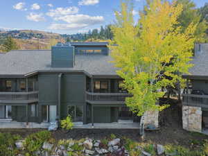 Rear view of house featuring a patio, a shingled roof, and a balcony