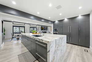 Kitchen with an island with sink, gray cabinets, modern cabinets, light wood-type flooring, and recessed lighting