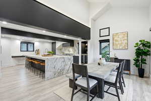 Dining area featuring light wood-style floors, a towering ceiling, and wine cooler