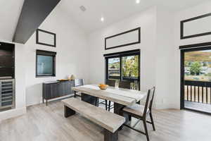 Dining space featuring high vaulted ceiling, light wood-style flooring, wine cooler, and recessed lighting