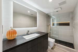 Full bathroom featuring vanity, tile walls, a walk in shower, and light wood-style flooring