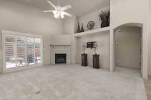 Unfurnished living room with a towering ceiling, arched walkways, light carpet, a fireplace, and ceiling fan