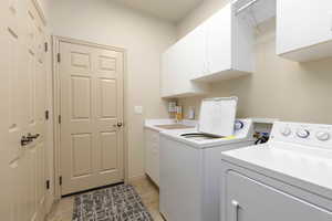 Laundry area with cabinet space, washing machine and clothes dryer, and light tile patterned floors