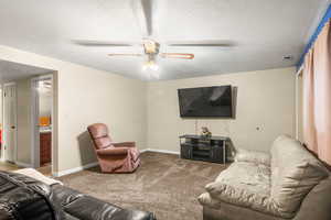 Living room featuring a textured ceiling, carpet floors, and a ceiling fan