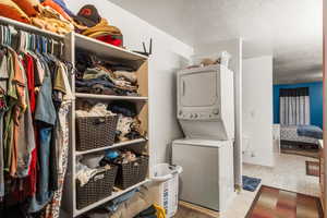 Washroom featuring a textured ceiling, stacked washer and clothes dryer, and light tile patterned floors