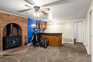 Indoor bar featuring a textured ceiling, a wood stove, dark countertops, dark carpet, and brown cabinetry
