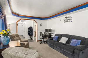 Living area featuring a textured ceiling, an office area, arched walkways, and a raised ceiling