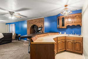 Kitchen with brown cabinetry, glass insert cabinets, a peninsula, a textured ceiling, and open floor plan