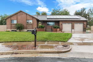 Ranch-style house with a front yard, solar panels, concrete driveway, brick siding, and roof with shingles