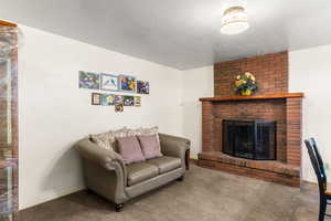 Carpeted living room featuring a brick fireplace and a textured ceiling