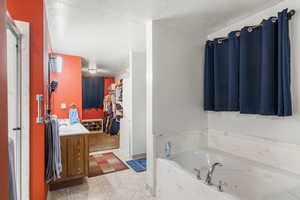 Bathroom with a walk in closet, a textured ceiling, vanity, and a jetted tub