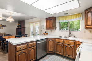 Kitchen with white electric range, a peninsula, light countertops, stainless steel dishwasher, and brown cabinetry