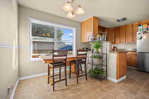Kitchen featuring pendant lighting, brown cabinetry, freestanding refrigerator, dark stone counters, and a chandelier