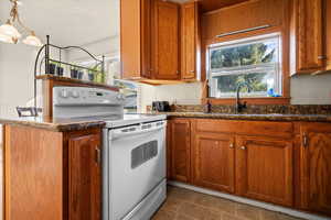 Kitchen featuring white range with electric cooktop, brown cabinetry, dark stone countertops, a peninsula, and pendant lighting