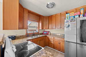 Kitchen with smart refrigerator, electric range oven, brown cabinets, a textured ceiling, and dark stone counters