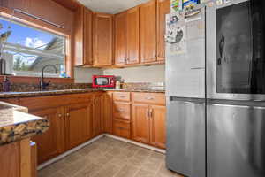Kitchen featuring smart refrigerator, dark stone counters, and brown cabinetry