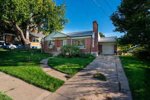 View of front of property with brick siding, a chimney, a front lawn, driveway, and a garage