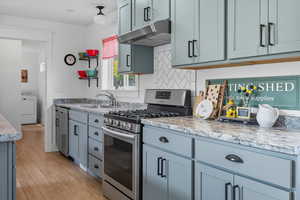Kitchen featuring stainless steel appliances, under cabinet range hood, light countertops, decorative backsplash, and washer / dryer