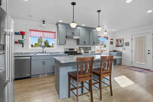 Kitchen featuring appliances with stainless steel finishes, a breakfast bar, gray cabinetry, a center island, and light wood-type flooring