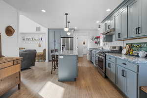 Kitchen with a breakfast bar area, a kitchen island, stainless steel appliances, gray cabinetry, and decorative light fixtures