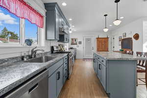 Kitchen with a kitchen breakfast bar, gray cabinetry, stainless steel appliances, light wood finished floors, and hanging light fixtures