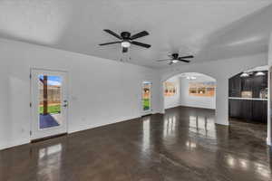 Unfurnished living room with ceiling fan, a textured ceiling, a chandelier, and arched walkways