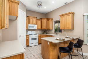 Kitchen with white appliances, light tile patterned floors, light countertops, a peninsula, and a kitchen breakfast bar
