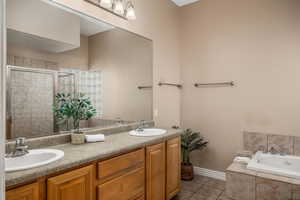 Full bath featuring a bath, double vanity, light tile patterned floors, and a shower stall
