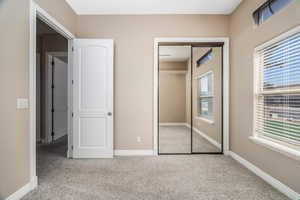 Unfurnished bedroom featuring light carpet, multiple windows, and a closet