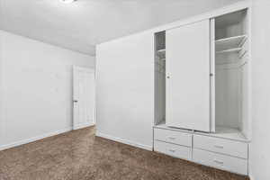 Unfurnished bedroom with dark carpet, a textured ceiling, and a closet