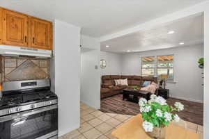 Kitchen featuring gas stove, tasteful backsplash, light tile patterned floors, under cabinet range hood, and brown cabinets