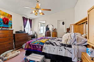 Carpeted bedroom featuring a textured ceiling, lofted ceiling, and ceiling fan