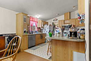 Kitchen with a peninsula, a breakfast bar, vaulted ceiling, a textured ceiling, and stainless steel appliances