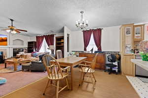 Dining area featuring a chandelier, a fireplace, a textured ceiling, light wood finished floors, and ceiling fan