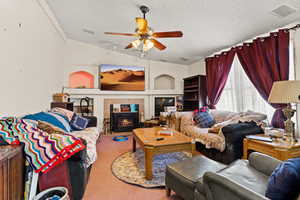 Living room with lofted ceiling, carpet, a textured ceiling, a fireplace, and ceiling fan