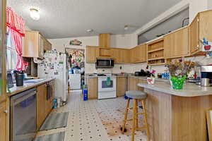 Kitchen featuring stainless steel appliances, a kitchen bar, light countertops, open shelves, and a peninsula