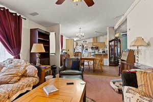 Living area featuring lofted ceiling, a ceiling fan, light wood-type flooring, a chandelier, and a textured ceiling