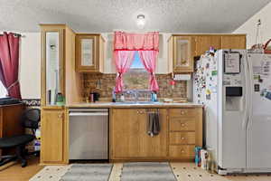 Kitchen featuring white fridge with ice dispenser, light countertops, a textured ceiling, dishwasher, and backsplash