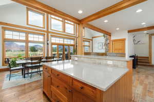 Kitchen with beamed ceiling, light stone countertops, brown cabinetry, a kitchen island, and light wood-style floors