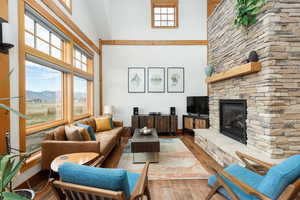 Living area featuring wood finished floors, a stone fireplace, a towering ceiling, and healthy amount of natural light