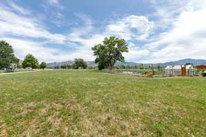 View of grassy yard with a mountain view, a greenhouse, a view of rural / pastoral area, an outbuilding, and a vegetable garden