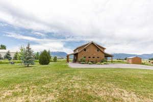Rear view of property featuring a mountain view, a yard, driveway, and an outdoor structure