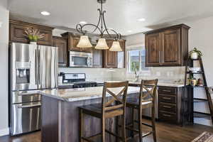 Kitchen with appliances with stainless steel finishes, dark brown cabinets, decorative light fixtures, a kitchen island, and a textured ceiling