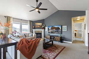 Living room featuring light carpet, a tile fireplace, vaulted ceiling, and ceiling fan