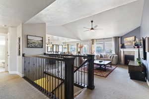 Living area featuring light colored carpet, vaulted ceiling, a fireplace with flush hearth, a ceiling fan, and a textured ceiling